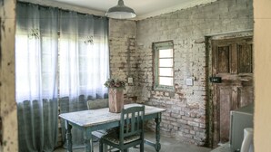 A rustic room with a wooden table and chairs, a brick wall, a window, and a door. - The Green Acorn Guest House (Setsoto)