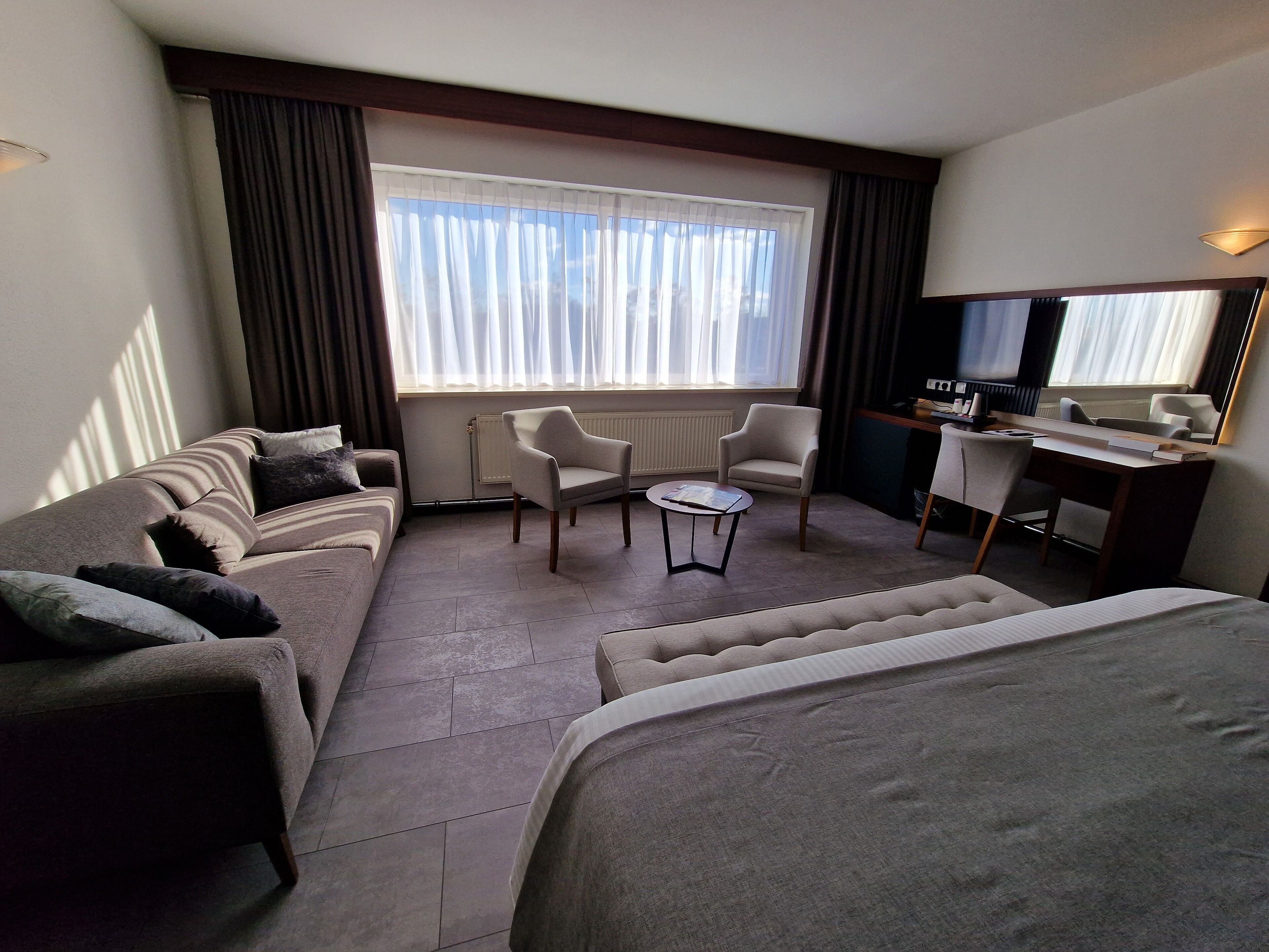Habitación de hotel con sofá, sillón, pequeña mesa y cama.