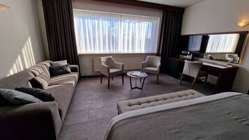 Habitación de hotel con sofá, sillón, pequeña mesa y cama.