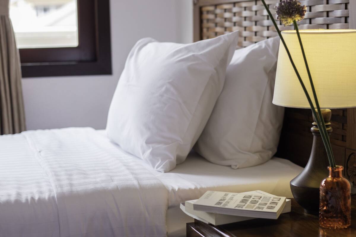 Un letto rifatto con lenzuola bianche, una lampada da comodino e un vaso con fiori.
