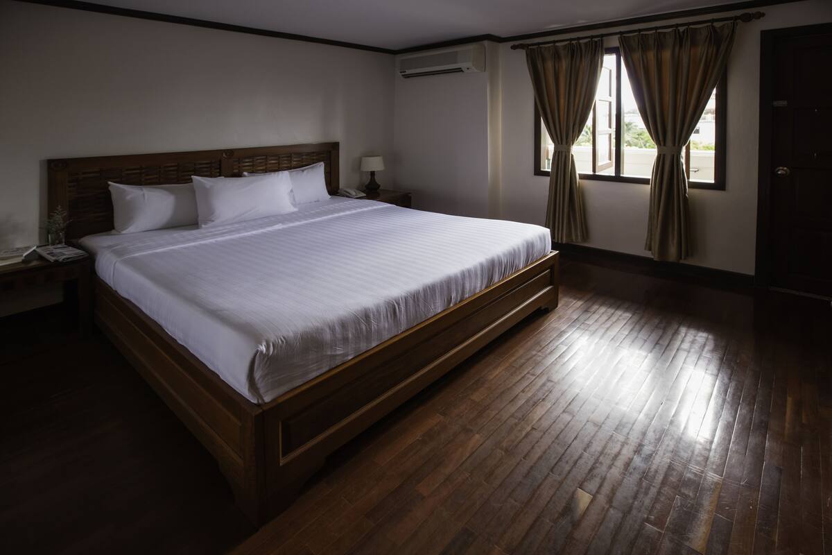Un letto grande con testiera in legno, un comodino con una lampada e una finestra con tende.