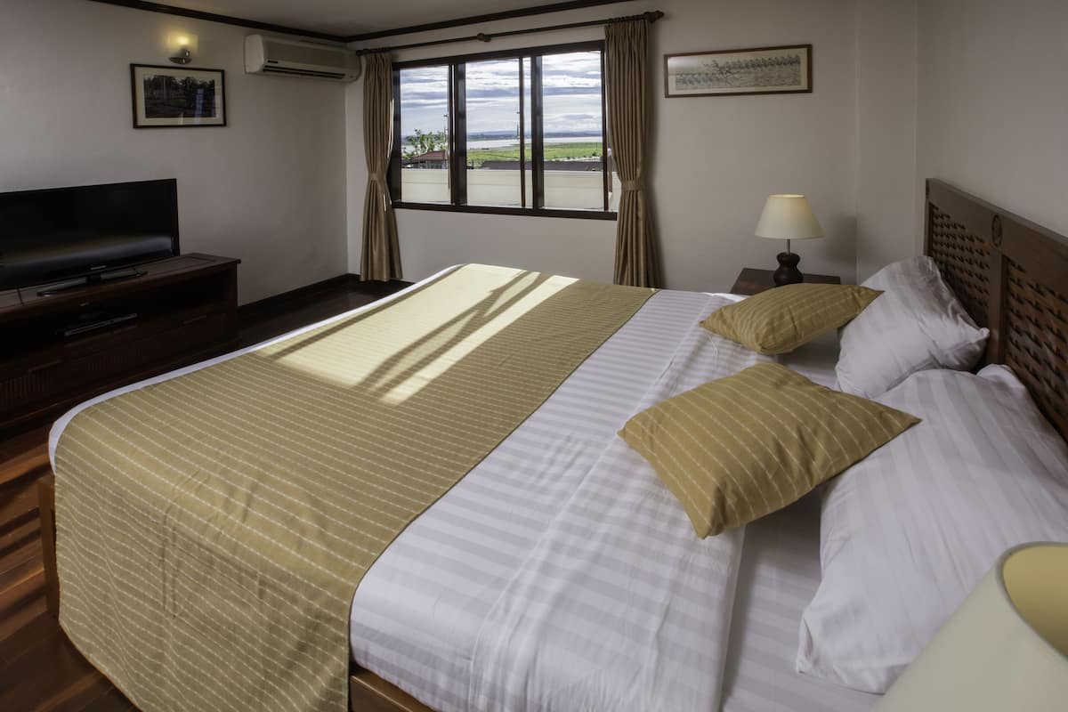 Una camera d'albergo con un letto grande, una televisione, una finestra con tende e una lampada.
