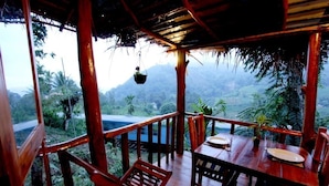 A wooden deck with a table and chairs, overlooking a mountainous landscape. - Ella Bamboo Cabana (Ella)