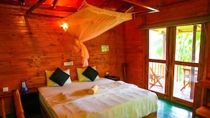 A wooden cabin room with a bed, pillows, a mosquito net, and a view of the outdoors. - Ella Bamboo Cabana (Ella)