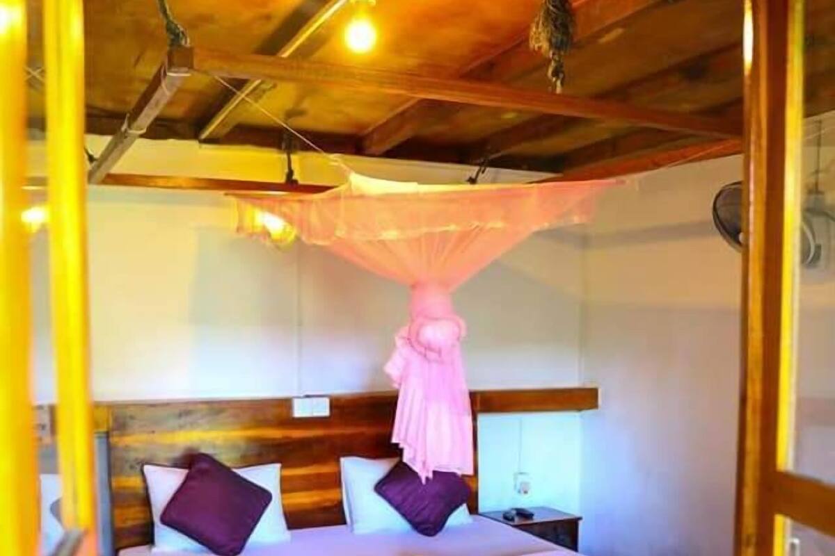 Un dormitorio con techo de madera, cama con ropa de cama blanca y morada, alfombra roja y mosquitera colgante.