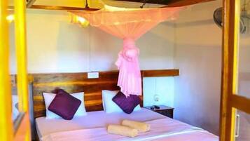 A bedroom with a wooden ceiling, a bed with white and purple bedding, a red rug, and a hanging mosquito net.
