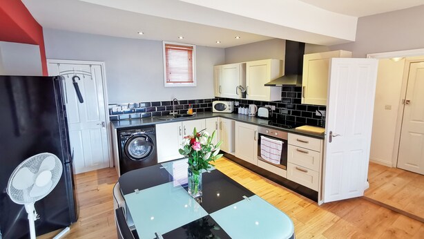 A compact kitchen with a microwave, toaster, and sink. There is a fan and a table with a vase of flowers. - Church View Apartments (Weymouth)