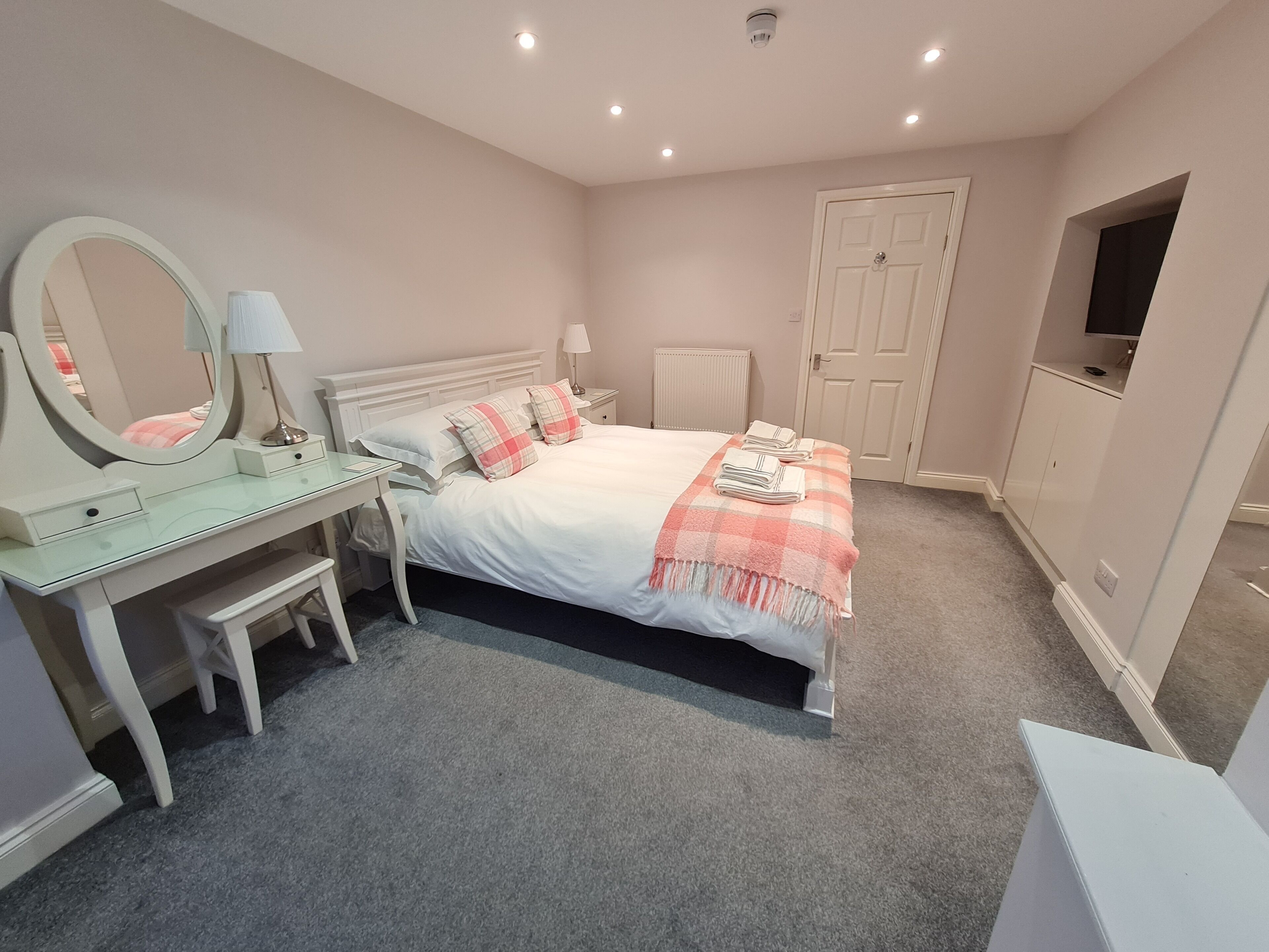 A bedroom with a bed, bedside tables, a mirror, a dresser, a radiator, and a television.
