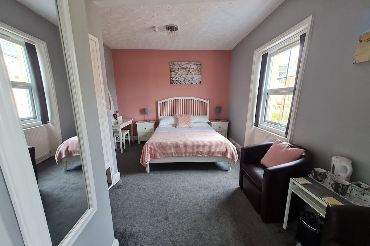 A bedroom with a bed, a desk, a chair, a nightstand, and a window.