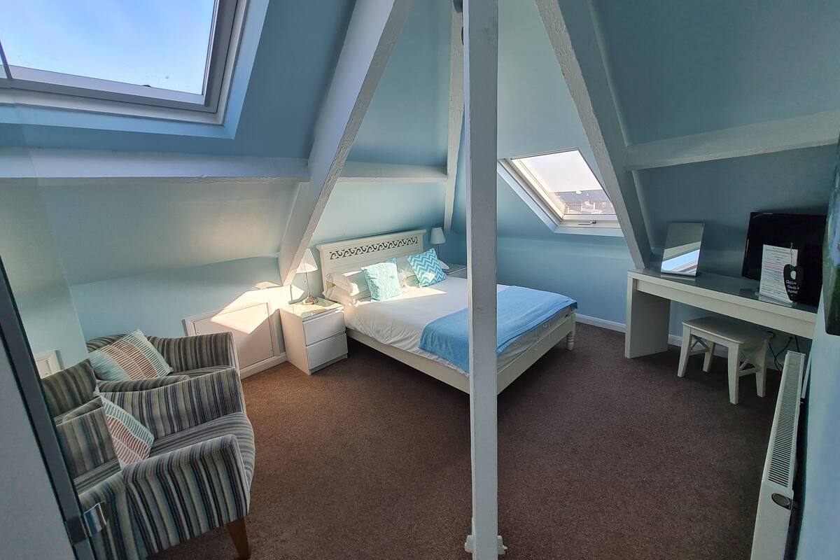 A bedroom with a sloped ceiling, a bed, a desk, and a chair.