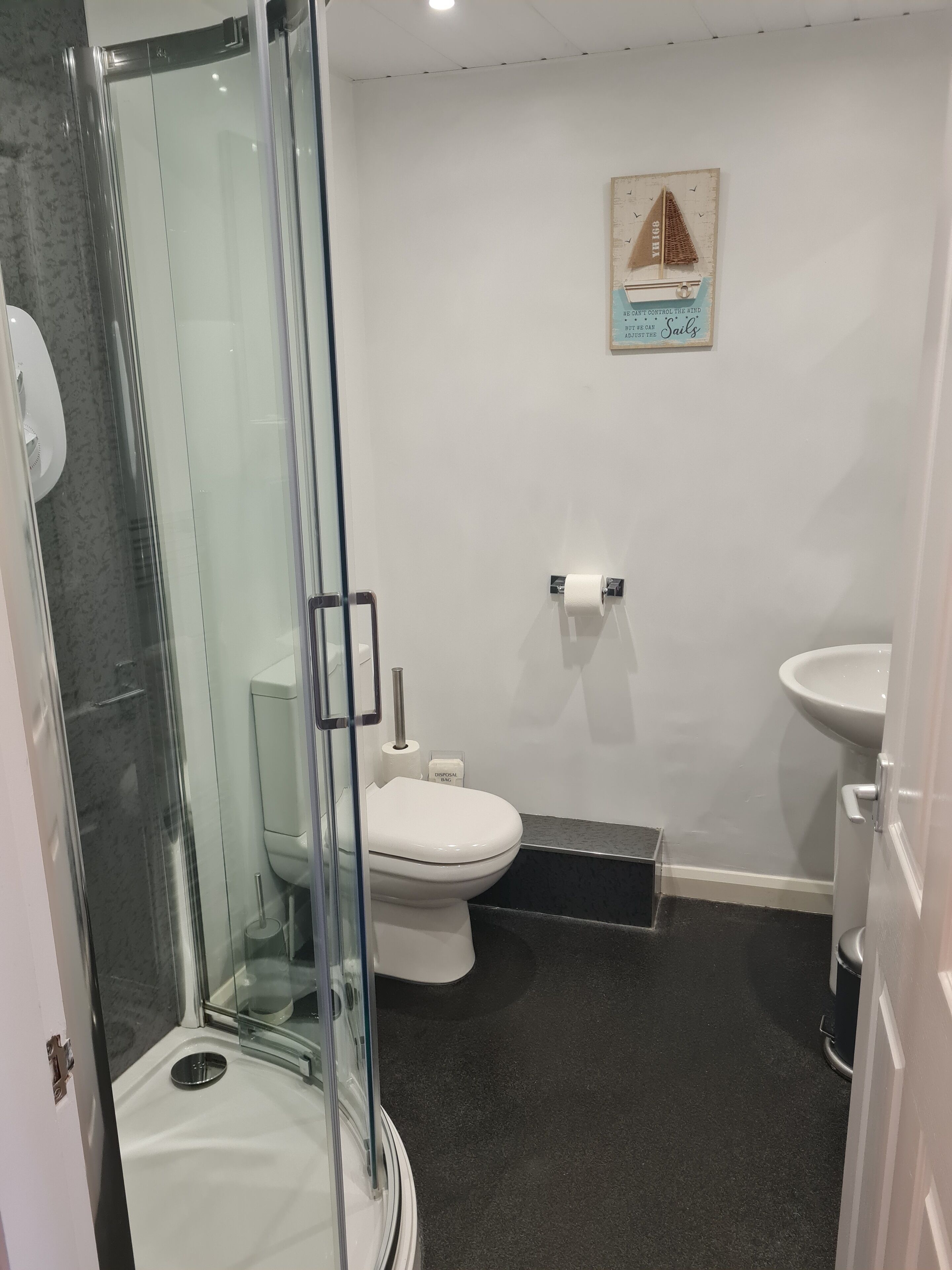 Un baño moderno con cabina de ducha de vidrio, inodoro, lavamanos y un cuadro enmarcado en la pared.