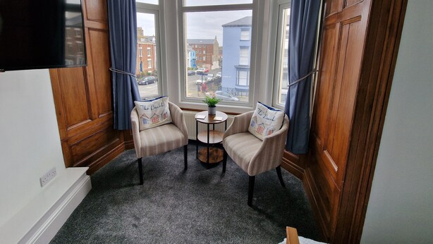 Habitación de esquina con dos sillones, una mesita y un televisor montado en la pared.