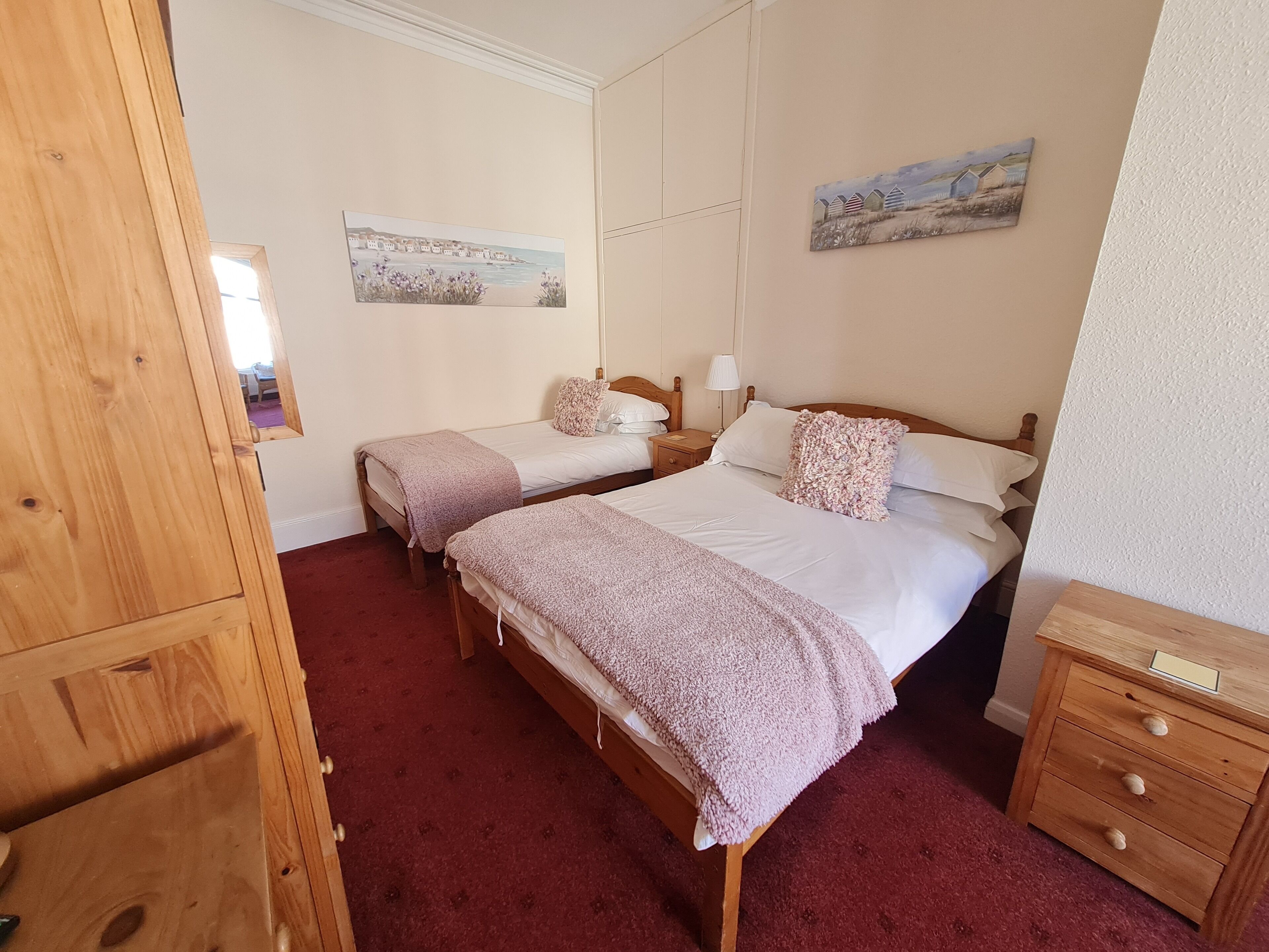 Una camera da letto con due letti singoli, un comodino in legno, una cassettiera e due quadri appesi al muro.