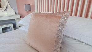 Una cama bien hecha con un almohadón grande, cuadrado y de color rosa claro con un borde de lentejuelas.