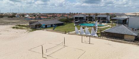 Une plage avec un terrain de volley-ball, une piscine et plusieurs bâtiments en arrière-plan.