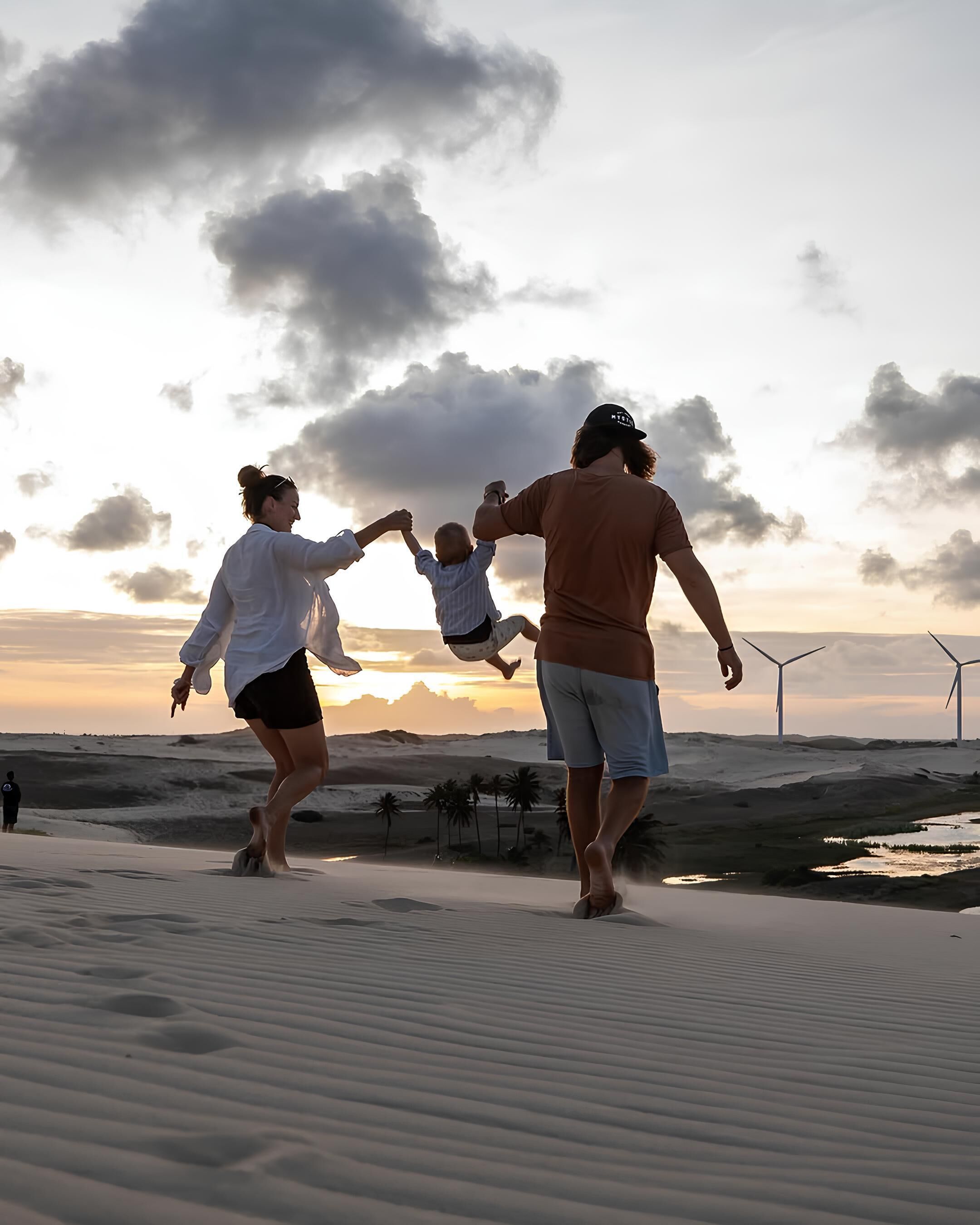 A family playing in sand dunes with wind turbines in the background.