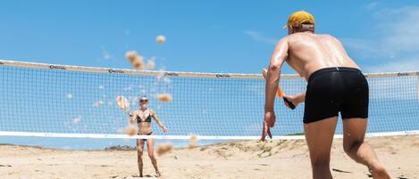 A beach volleyball game with players in black shorts and a yellow cap.