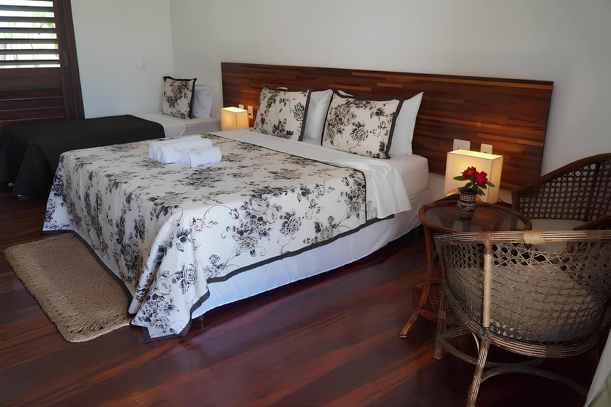 Une chambre avec un grand lit, deux tables de chevet avec des lampes, un fauteuil en osier et un plancher en bois.