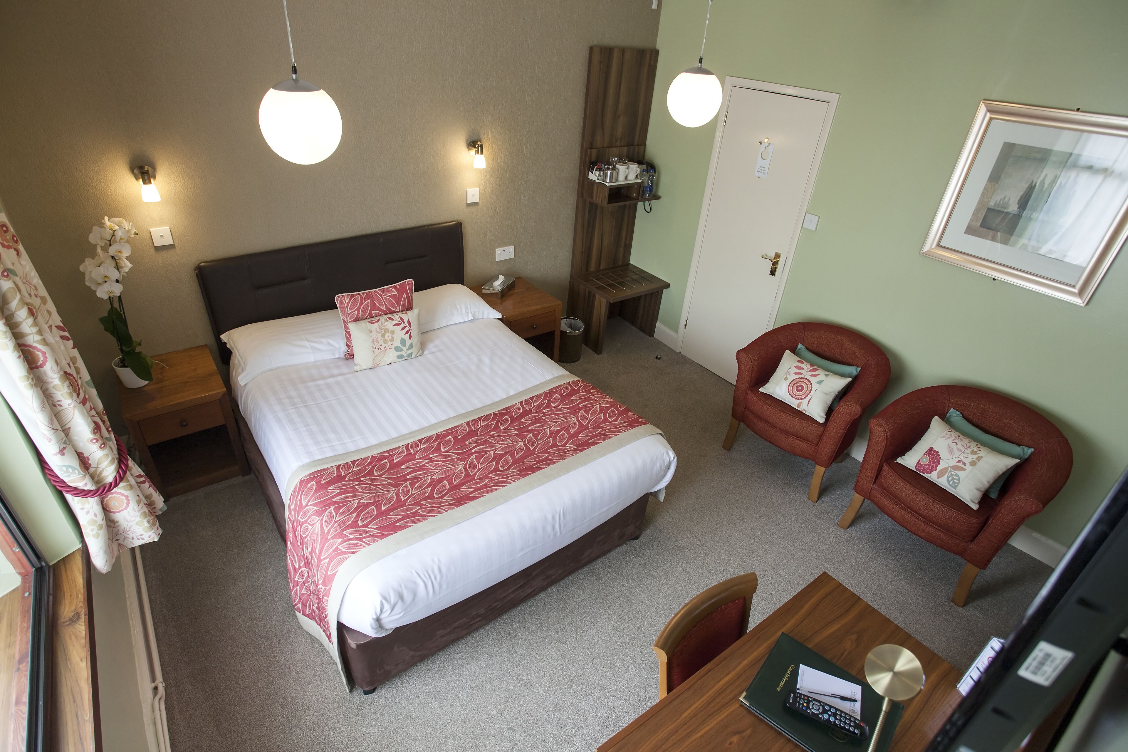 A hotel room with a large bed, two bedside tables, a desk with a chair, a TV, and a framed picture on the wall.