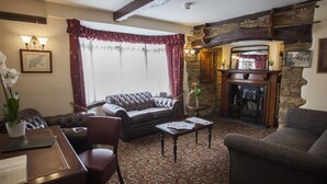 A cozy living room with a fireplace, leather sofas, a patterned carpet, and a dining area with a table and chairs. - The Poplars Moulton (Northampton)