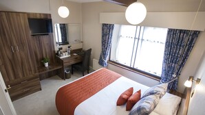 A bedroom with a bed, a desk, a chair, a television, and a window with curtains. - The Poplars Moulton (Northampton)