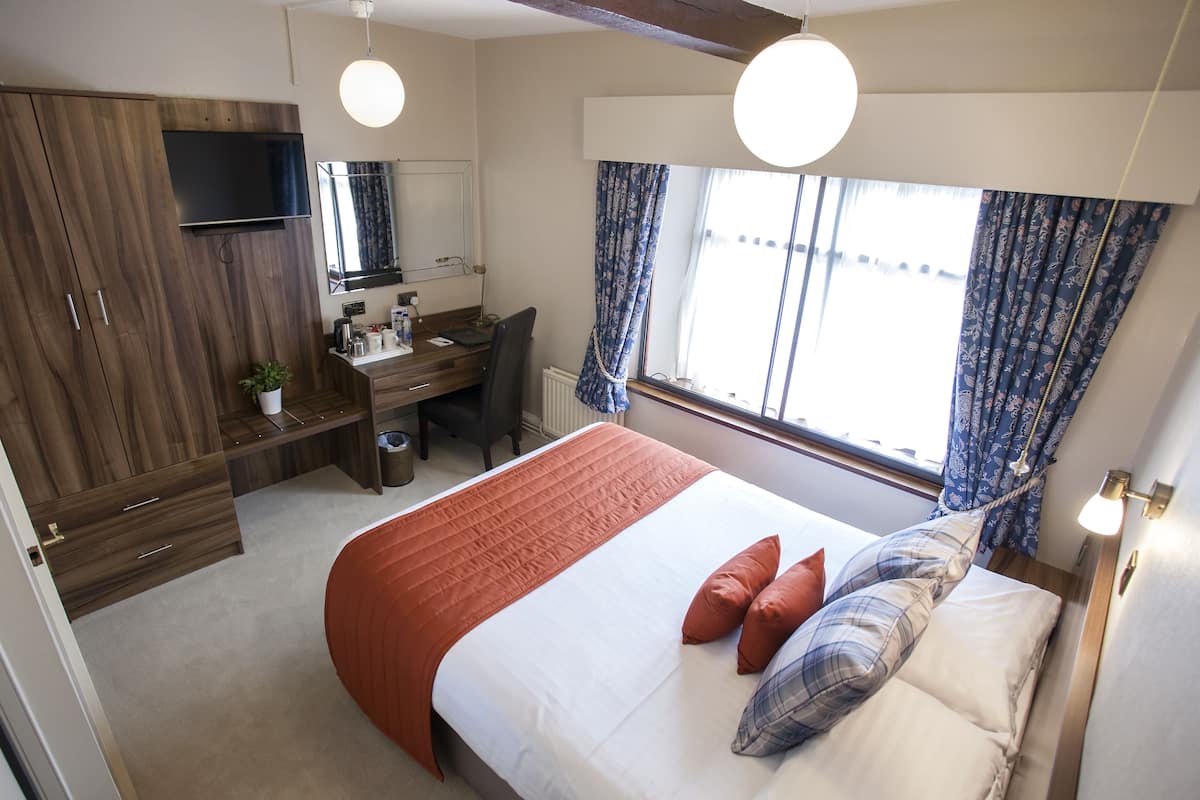 Ein Schlafzimmer mit einem Bett, einem Schreibtisch, einem Sessel, einem Fernseher und einem Fenster mit Vorhängen.