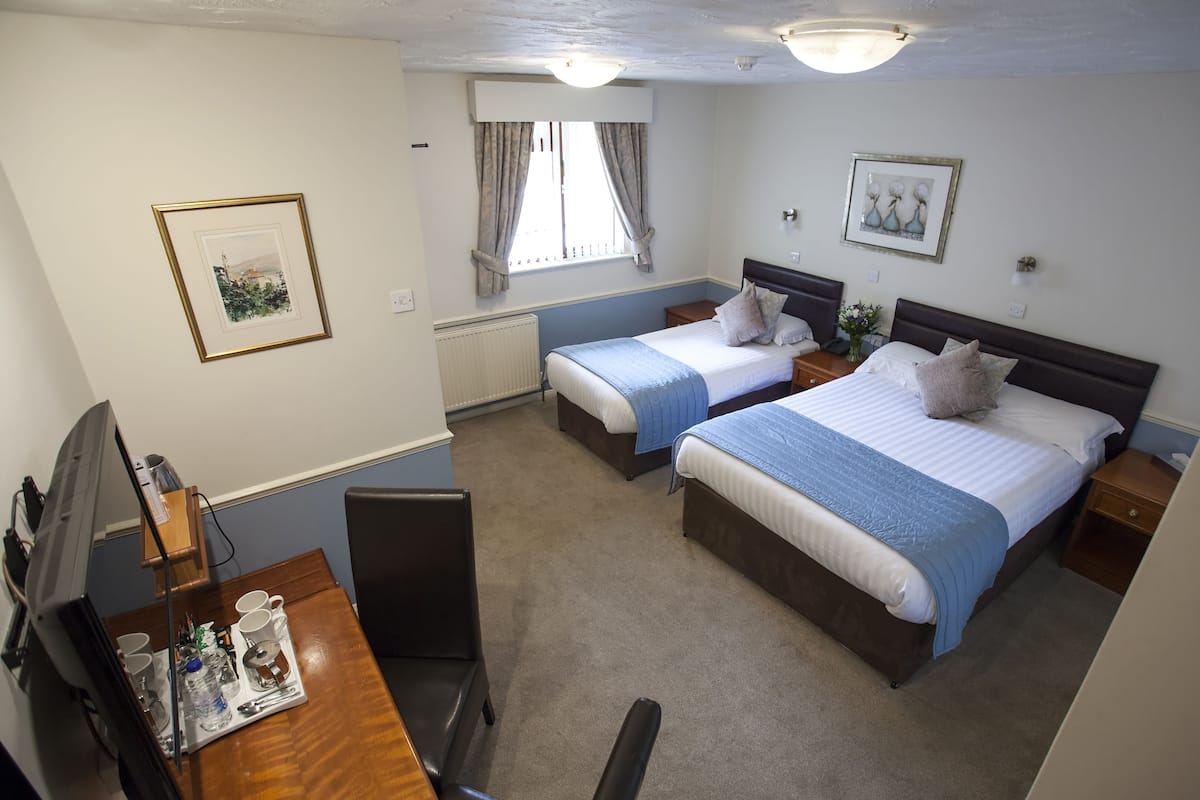 Ein Hotelzimmer mit zwei Einzelbetten, einem Schreibtisch mit Stuhl, einem Fernseher und einem Fenster mit Vorhängen.