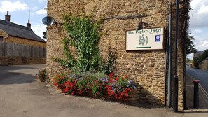 The Poplars Hotel sign on a stone wall with a satellite dish and ivy. - The Poplars Moulton (Northampton)