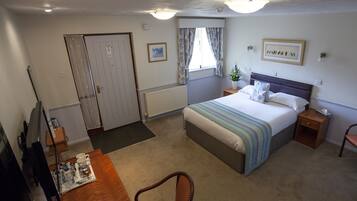 Ein Hotelzimmer mit Bett, Nachttisch, Stuhl, Schreibtisch und Fernseher.
