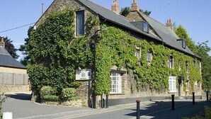 A stone building with ivy covering the walls, a sign indicating it is a hotel, and a clear road in front. - The Poplars Moulton (Northampton)