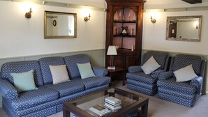 A living room with a patterned sofa, a matching armchair, a coffee table, and a wooden cabinet with shelves. - The Poplars Moulton (Northampton)