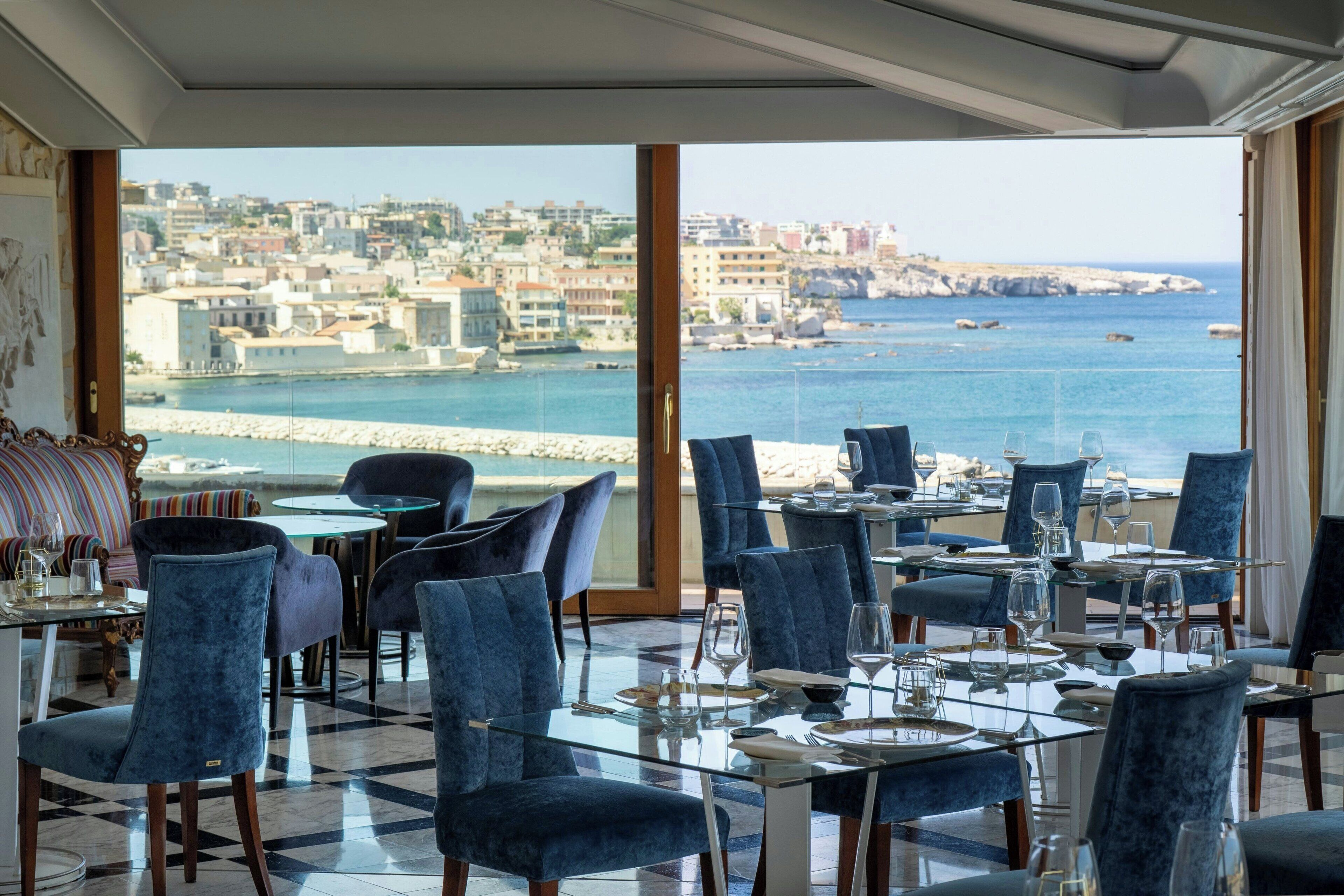 Un espace repas avec des tables et des chaises, une vue sur la mer et les bâtiments, et une grande fenêtre.