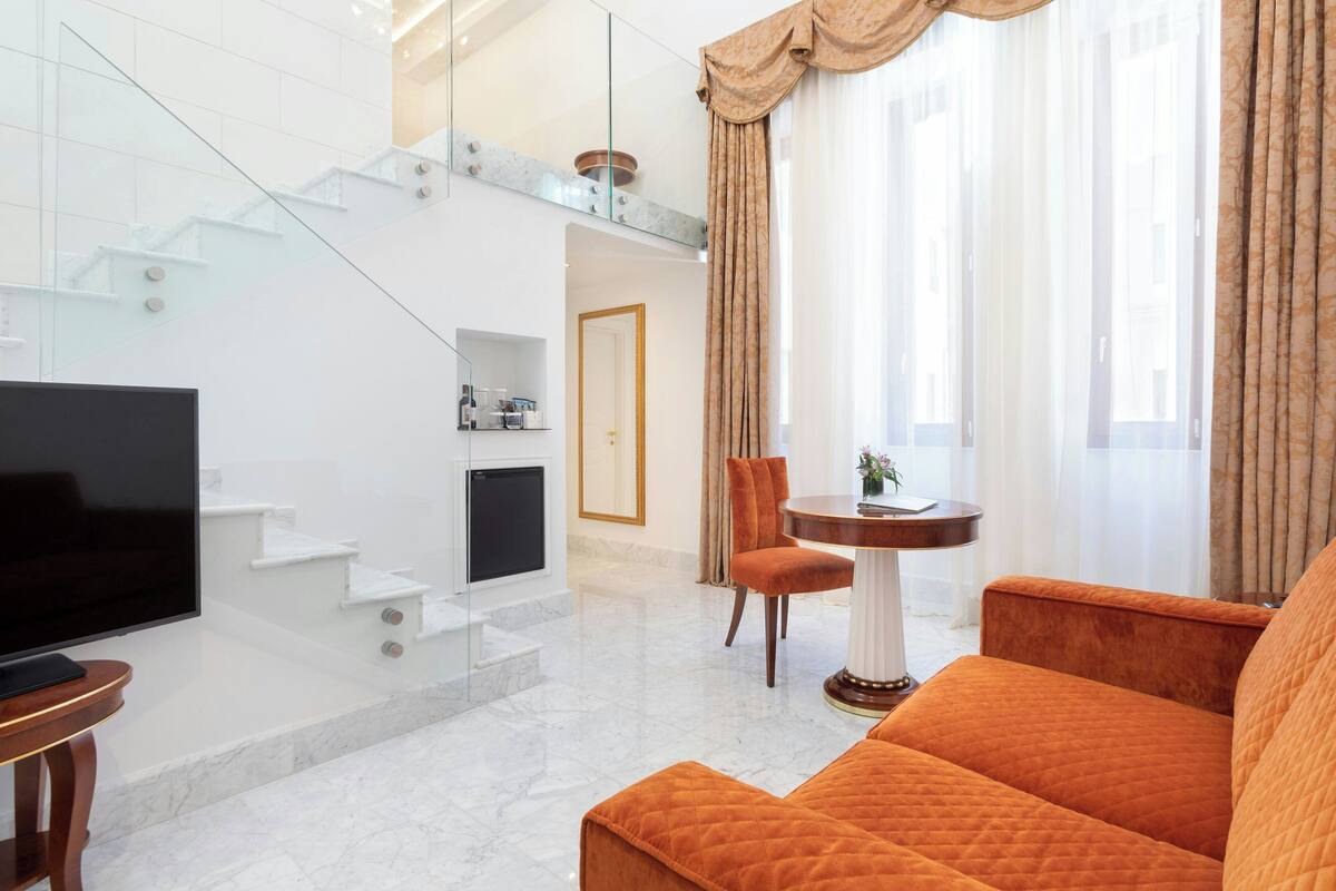 A modern living room with a flat-screen TV, a sofa, a dining table, and a staircase.