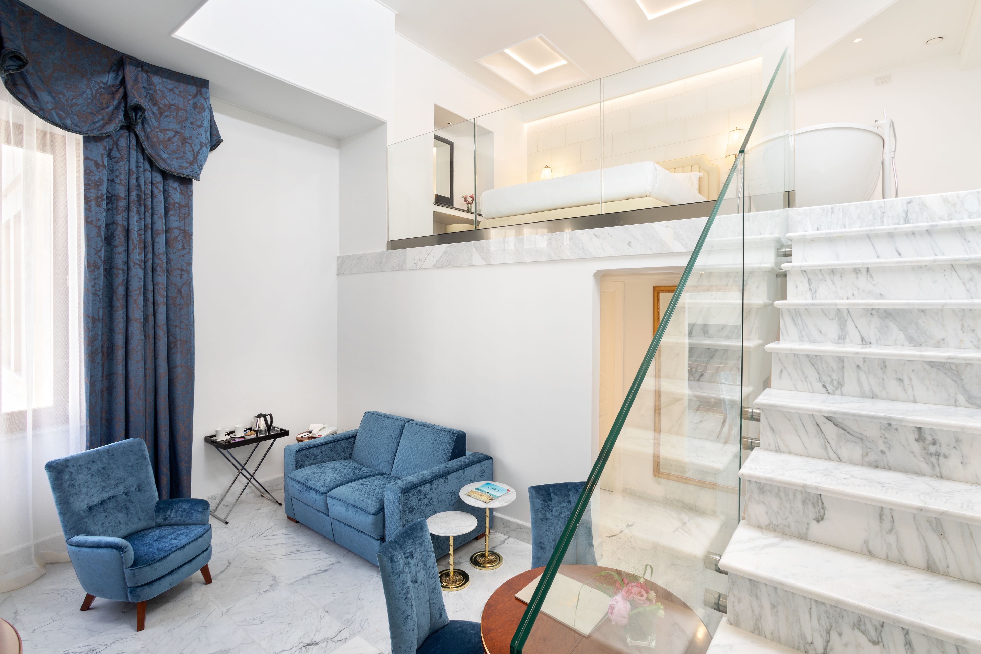 Un hall d’hôtel moderne avec un escalier en marbre, un ensemble de canapés bleus et une rambarde en verre.