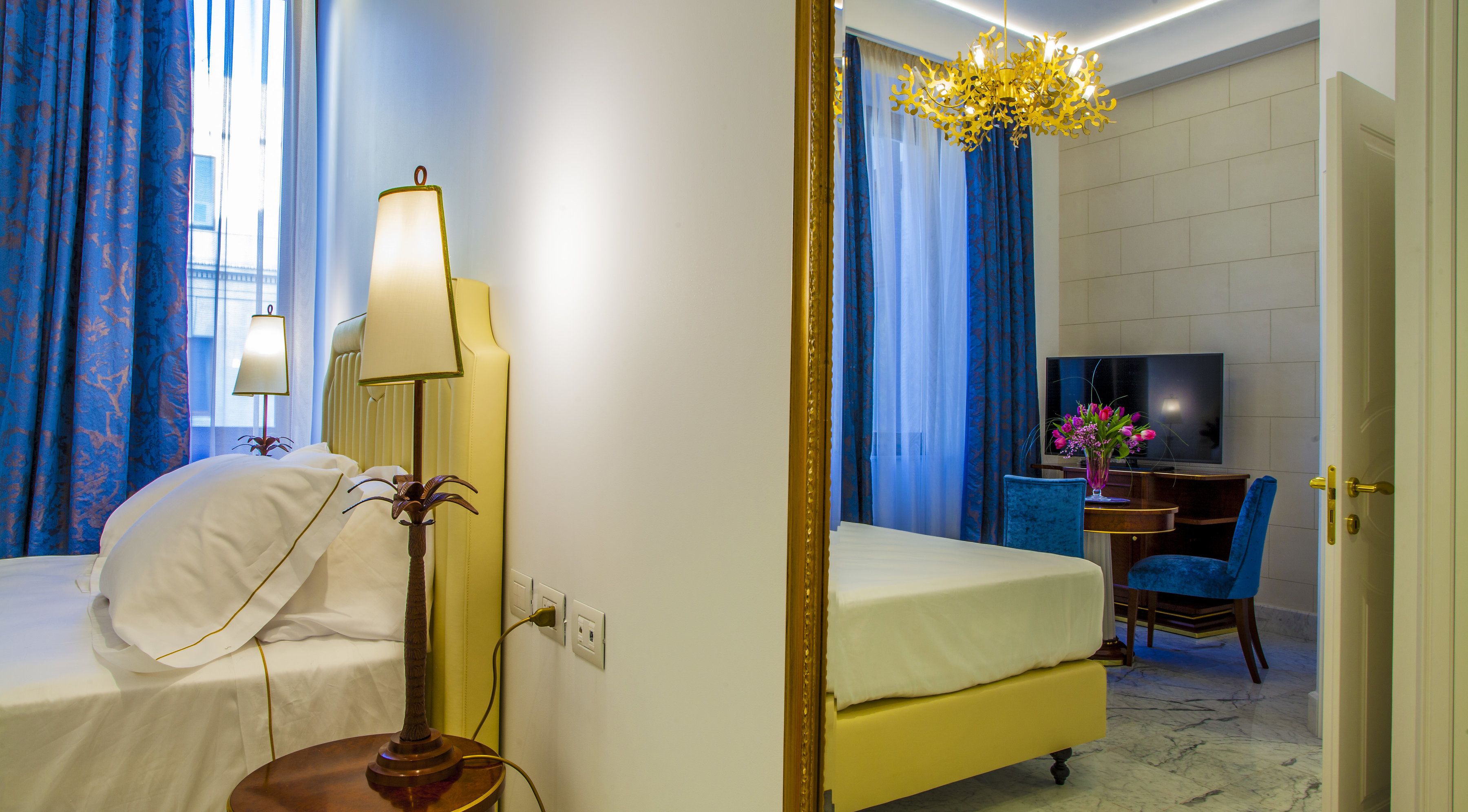 Een hotelkamer met een bed, bedlamp, televisie en een bureau met stoel.