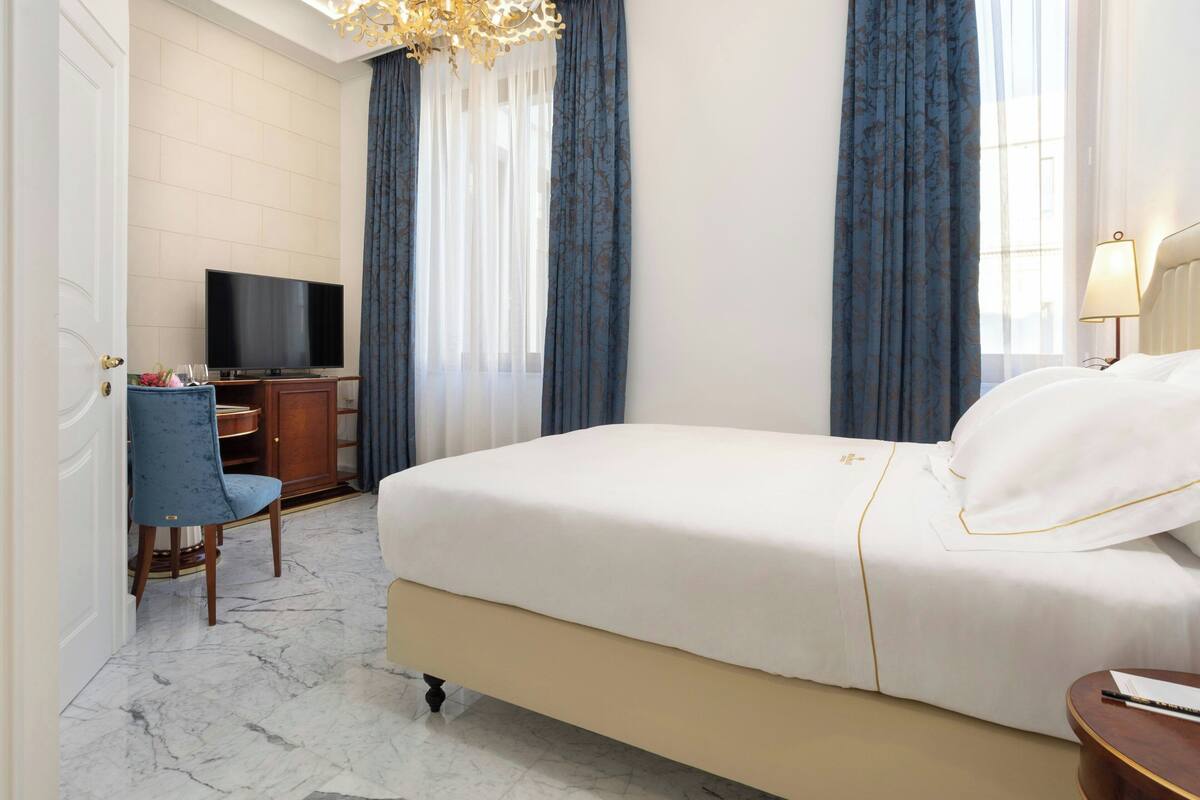 A hotel room with a bed, a desk with a television, a chair, and a lamp.