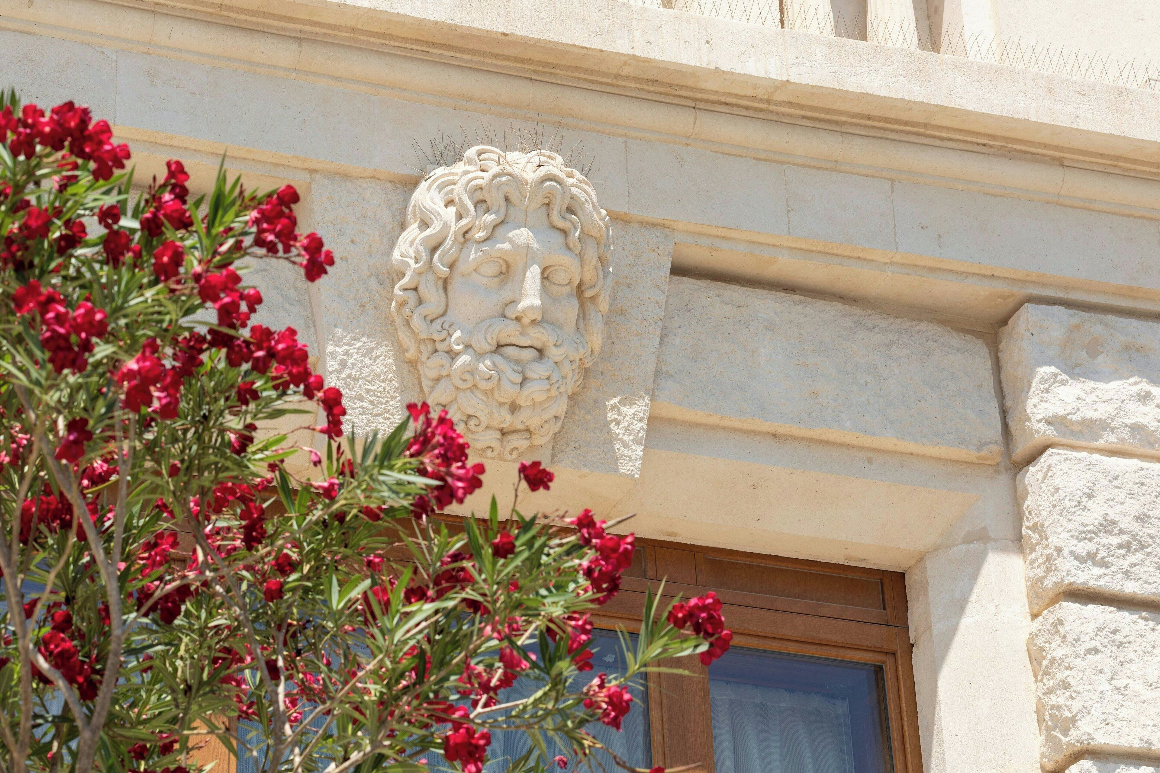 Une façade en pierre, ornée d’une tête de lion sculptée et d’une fenêtre à cadre en bois.