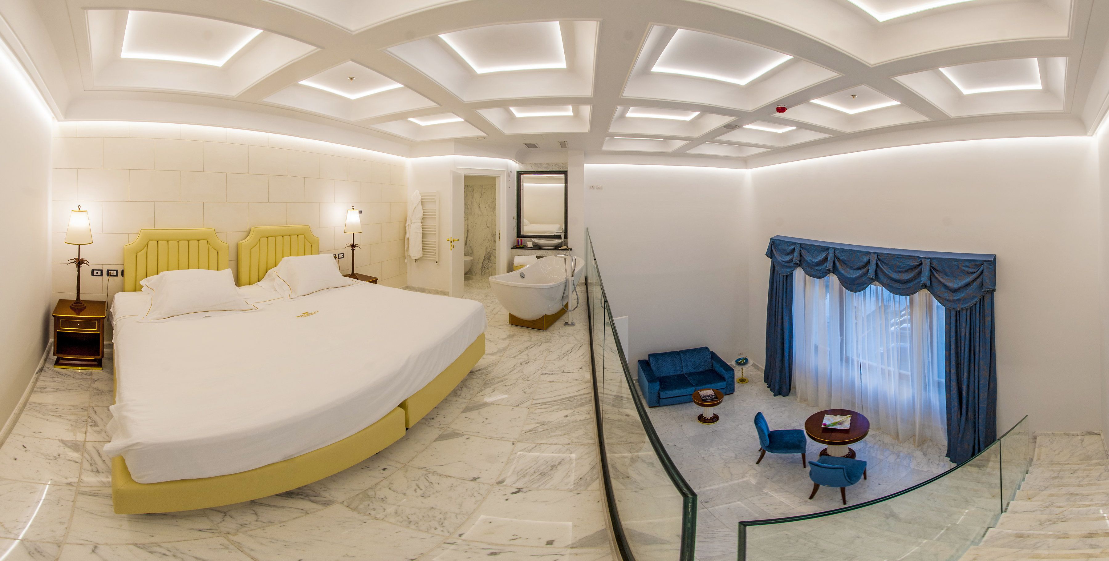 Ein modernes Hotelzimmer mit einem großen Bett, einem Badezimmer, einem Balkon mit Sitzgelegenheit und einer Glastrennwand.