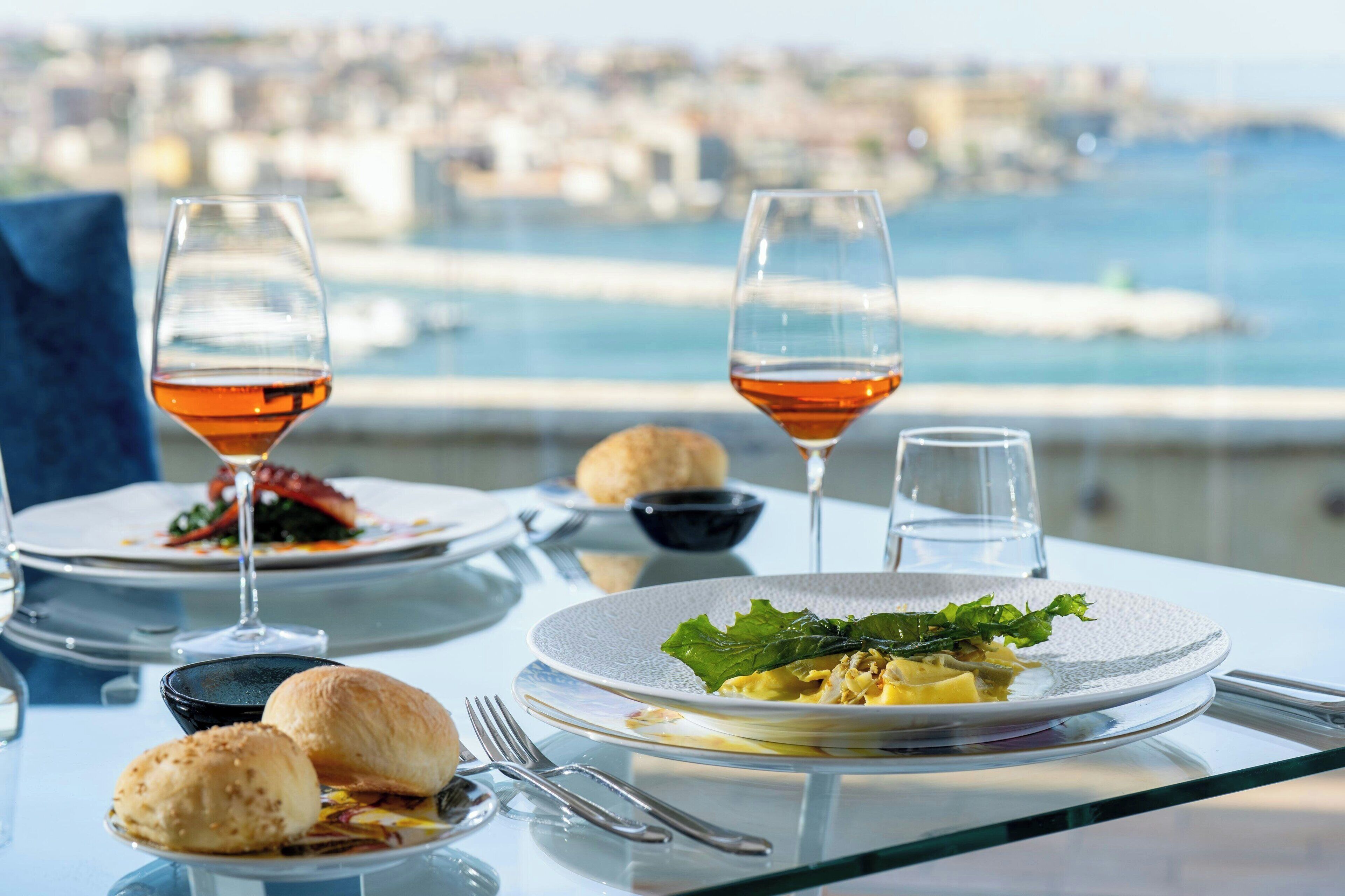 Una mesa con platos de comida, copas de vino y vista al mar.