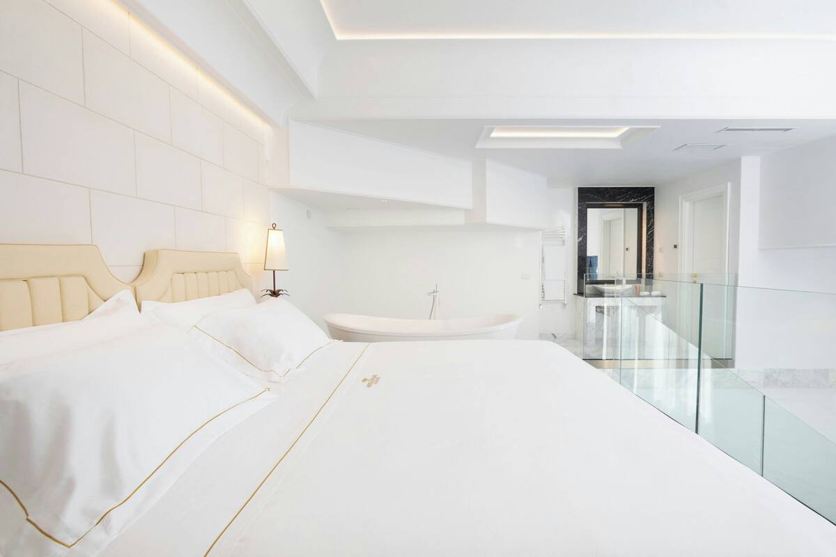 A modern hotel room with a large bed, a glass-enclosed bathroom, and a minimalist design.