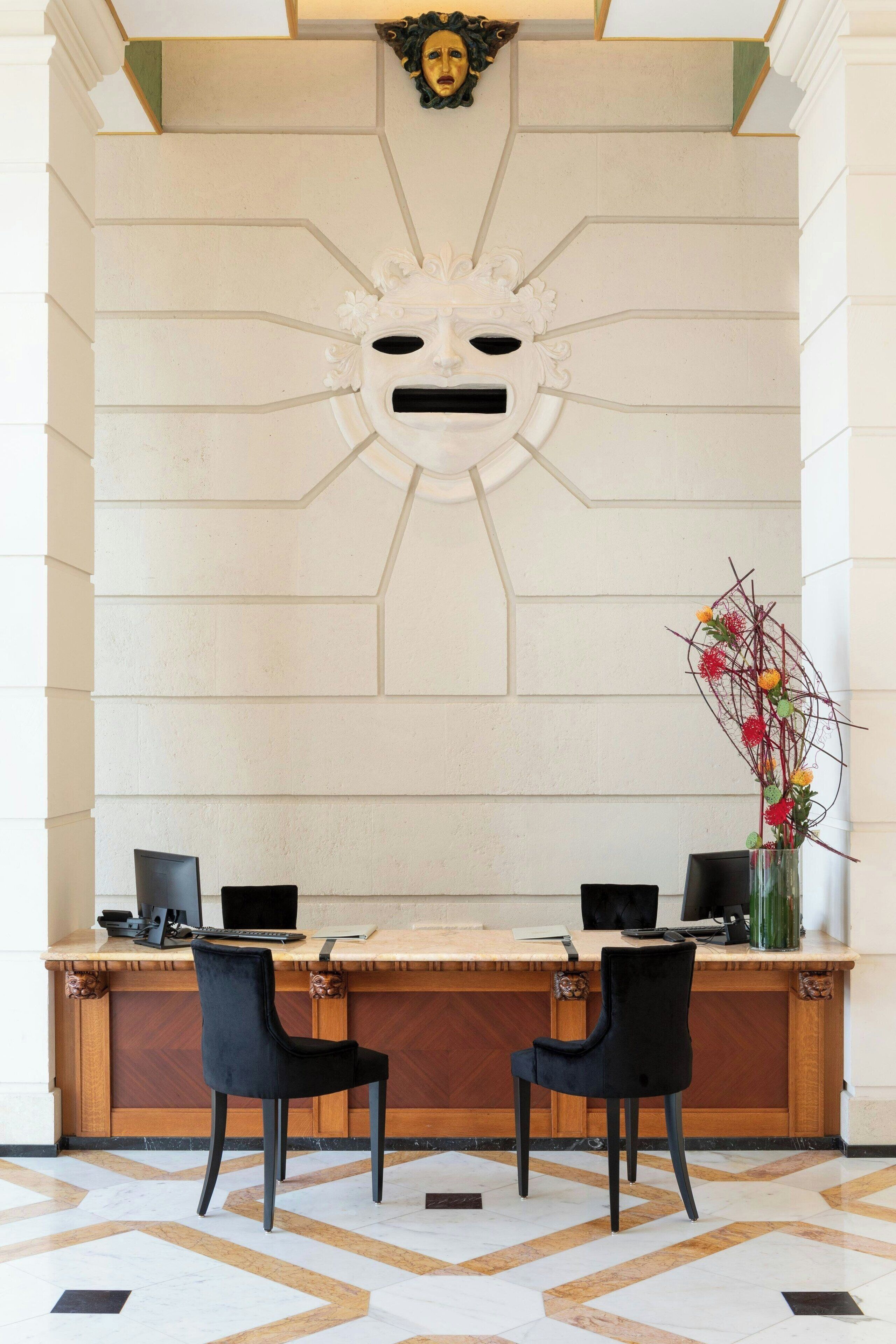 A reception desk with two black chairs, a wooden counter, and a decorative wall with a sun motif.