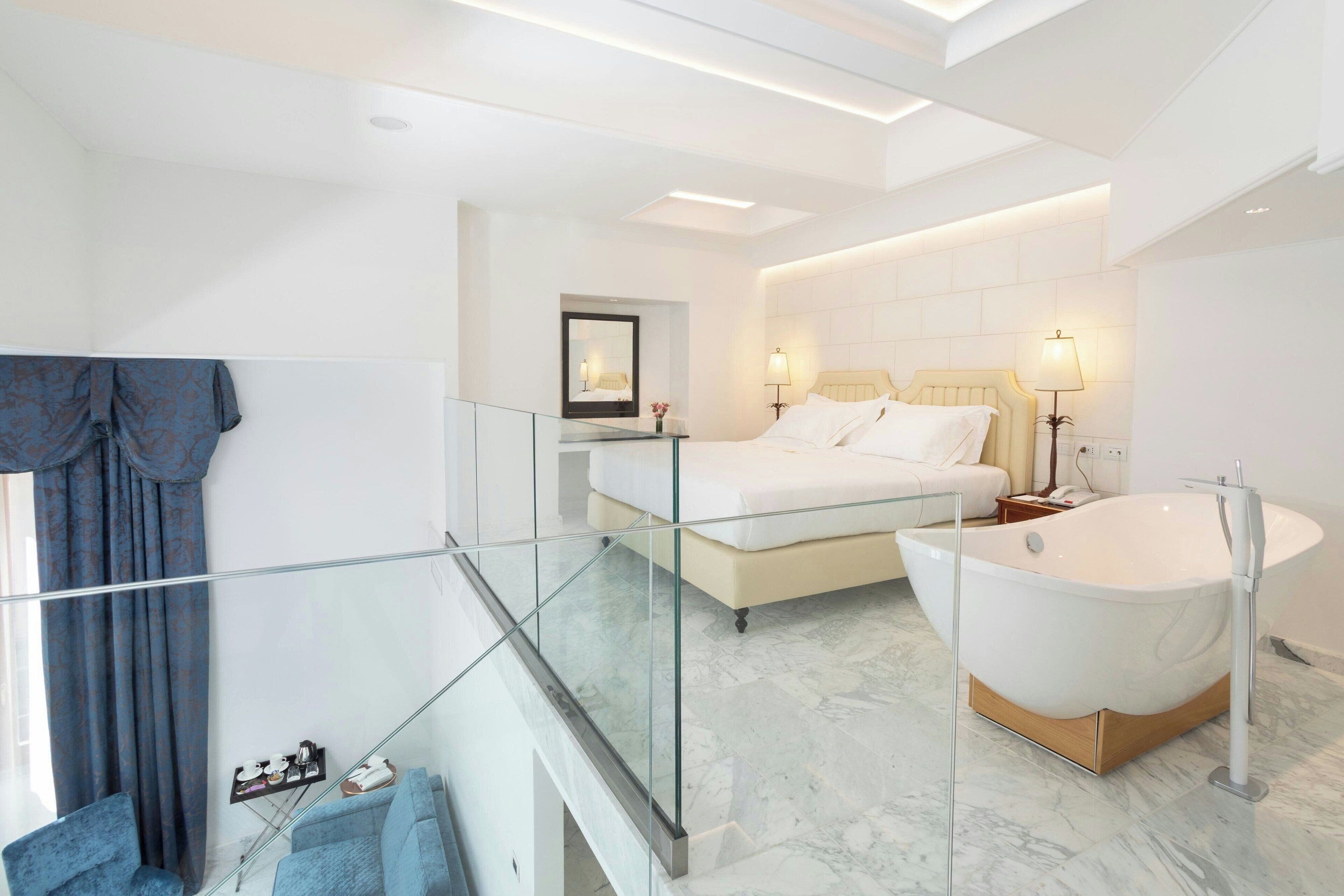 A modern bedroom with a glass balcony, a large bathtub, and a glass shower enclosure.