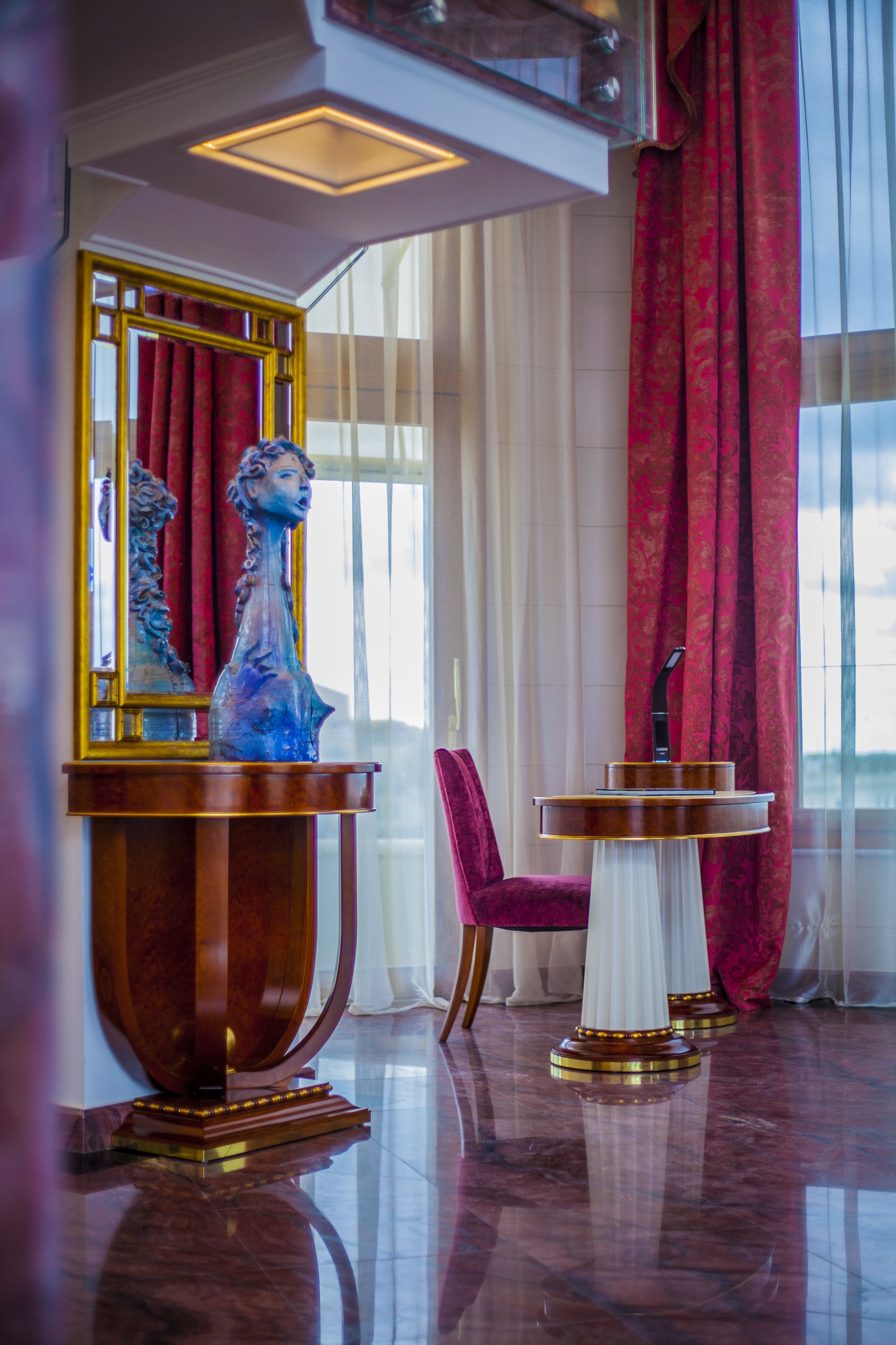 Un hall d’entrée luxueux avec un sol en marbre, un grand vase décoratif, une table ronde équipée d’un microphone et un rideau rouge.