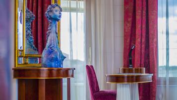Un hall d’entrée luxueux avec un sol en marbre, un grand vase décoratif, une table ronde équipée d’un microphone et un rideau rouge.