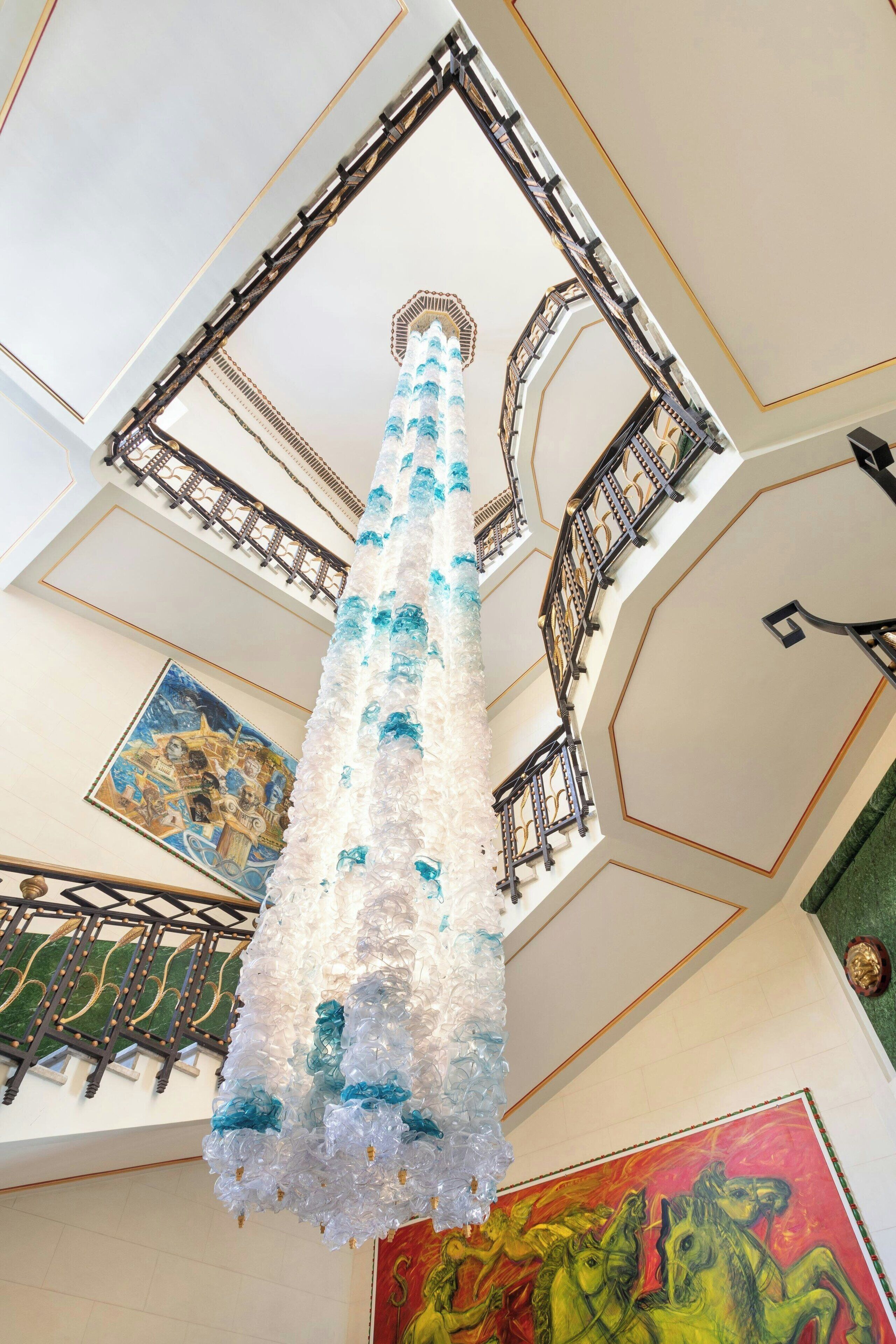 Un candelabro con diseño blanco y azul, un techo con adornos dorados y un cuadro de caballos.
