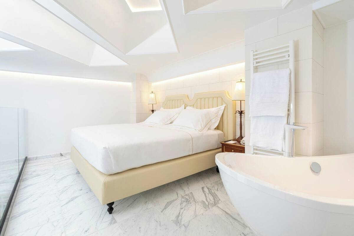 A modern bedroom with a large bed, a bathtub, and a glass shower enclosure.