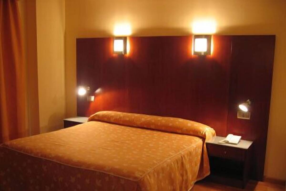 A hotel room with a large bed, two bedside tables, and two wall-mounted lamps.