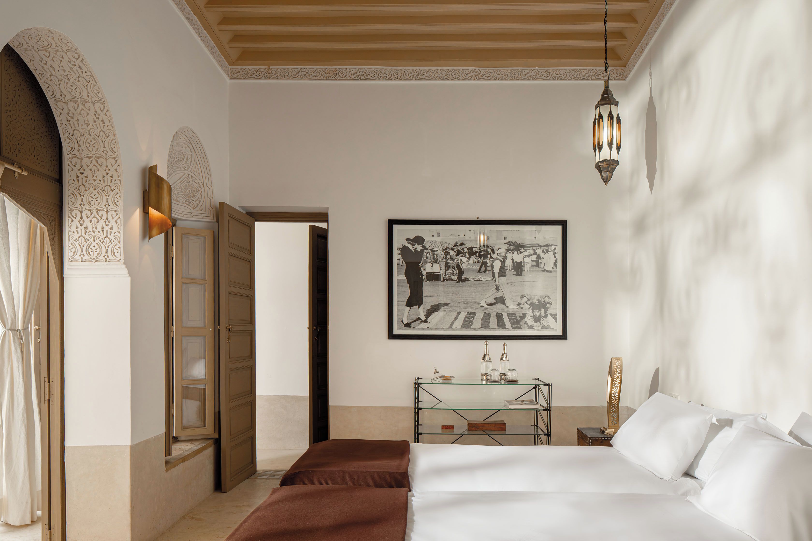 Een hotelkamer met een bed, een ingelijst schilderij aan de muur, een glazen bijzettafeltje en een deur met ingewikkelde versieringen.