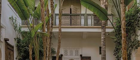 A courtyard with a pool, palm trees, and a traditional building with ornate doors and balconies.