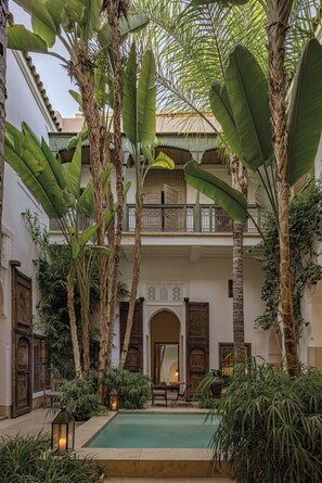 A courtyard with a pool, palm trees, and a traditional building with ornate doors and balconies. - Riad Jaaneman (Marrakech)